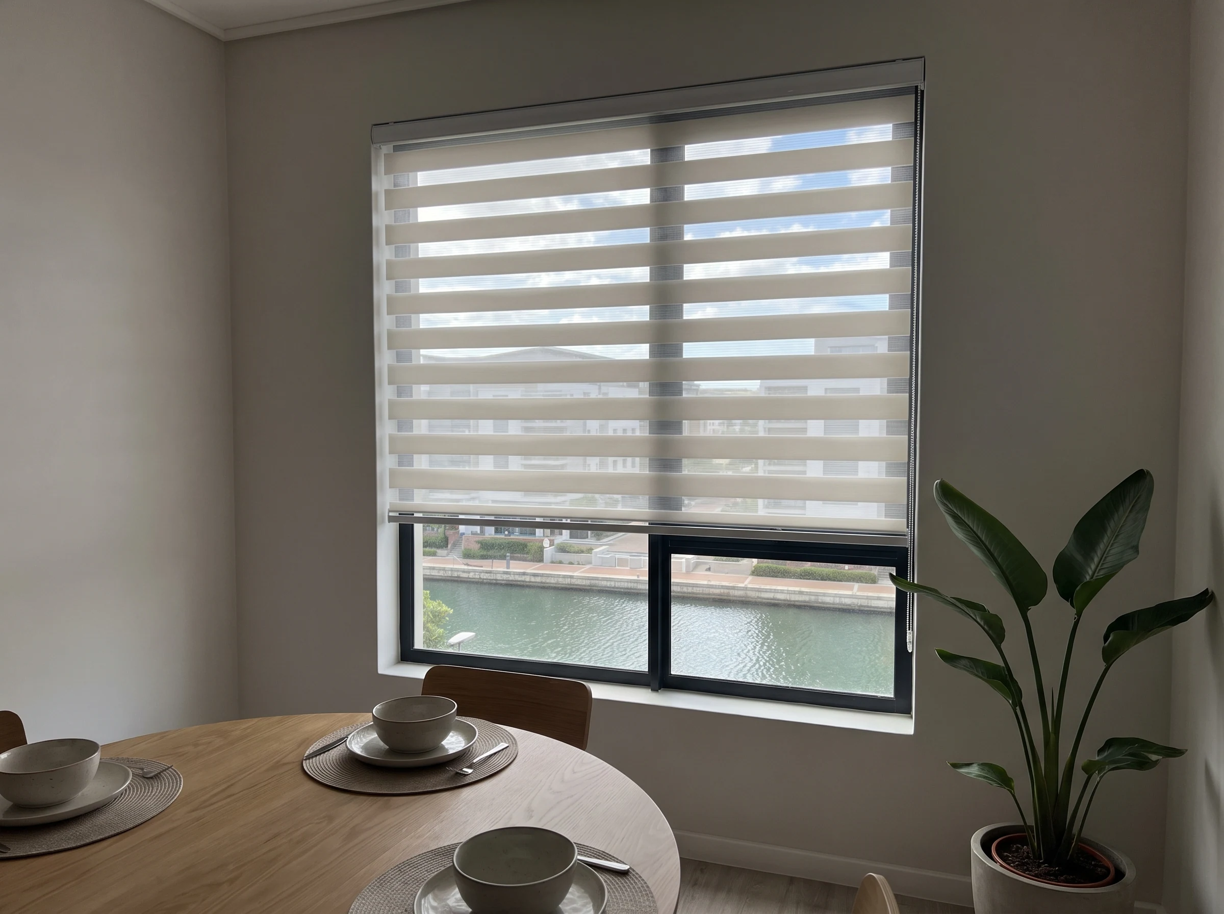 Day-night zebra blind with alternating sheer and solid bands in a Century City apartment dining area overlooking the canal
