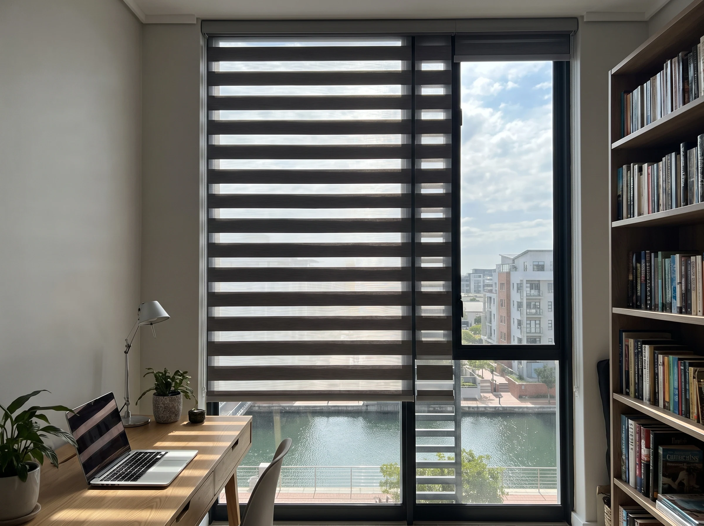 Day-and-night banded roller blind with alternating sheer and solid stripes on a tall window in a Century City apartment study, canal glimpse through the glass