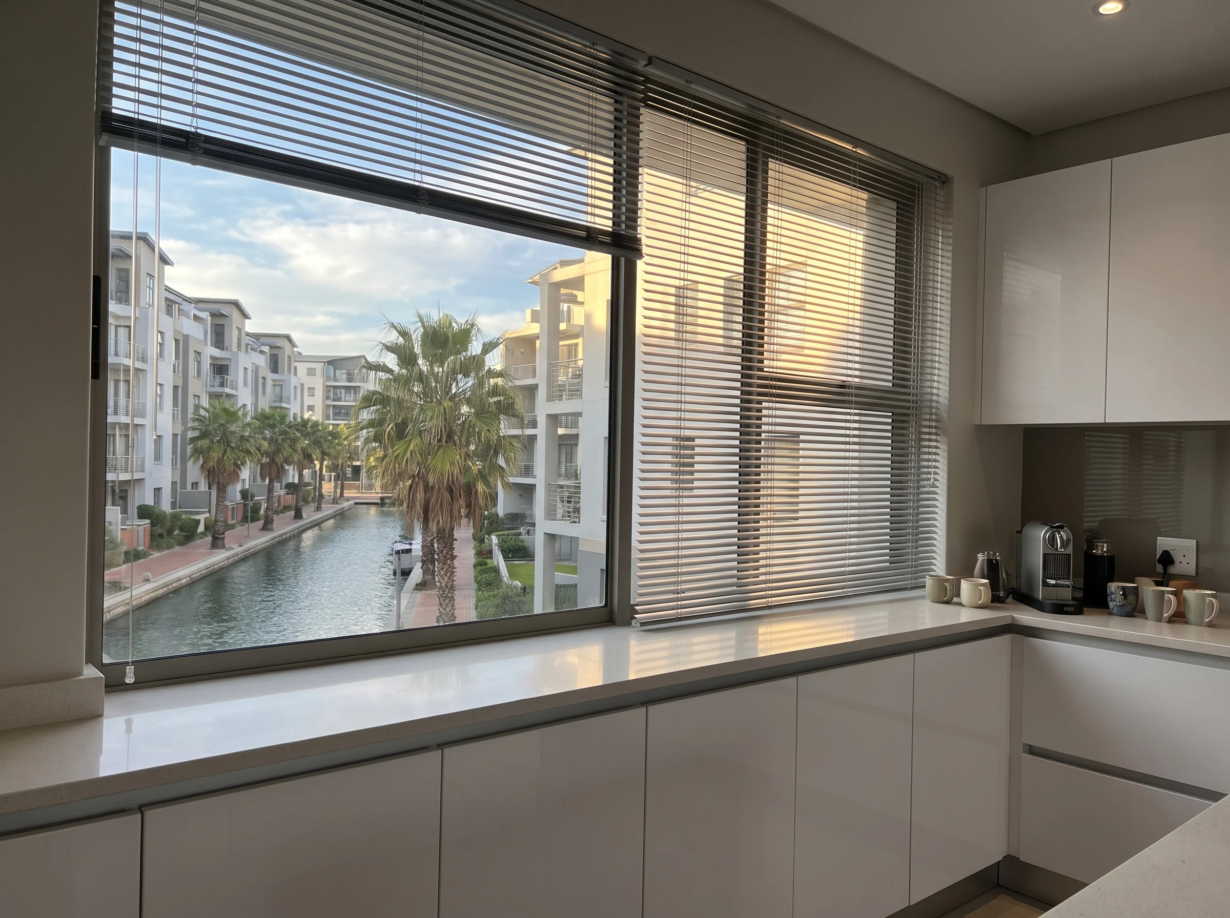 Slim aluminium venetian blind with tilted slats in a Century City apartment kitchen window overlooking a canal walkway